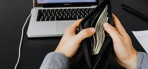 Person holding wallet in front of laptop showing charts, representing rising costs and website project budget overruns