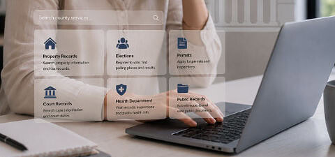 Woman using a laptop to access county government website services including property records, elections, permits, court records, and health department information